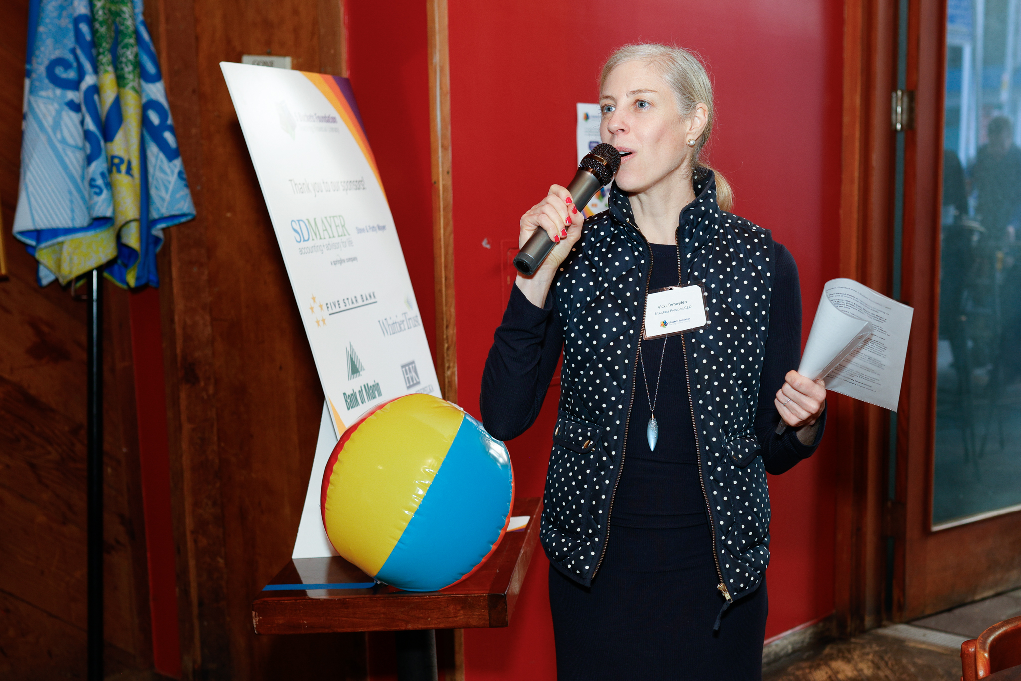 Vicki speaking into a microphone at a 5 Buckets fundraising event